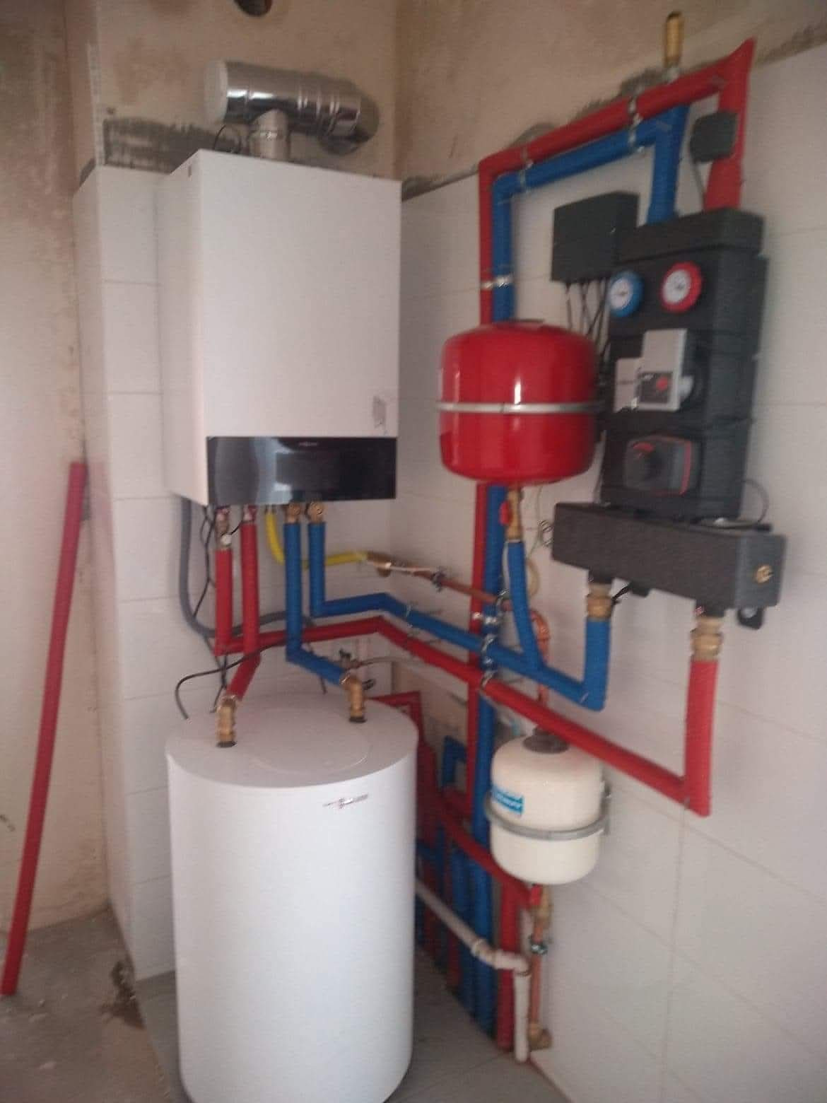 Nowoczesny piec gazowy Viessmann z czerwonym zbiornikiem wyrównawczym i niebiesko-czerwonymi rurami instalacji CO, zamontowany na tle surowej ściany.