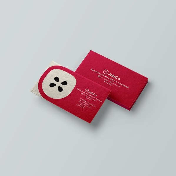 Dwie czerwone wizytówki firmy JabCo z logo w kształcie jabłka na szarym tle. Jedna wizytówka leży płasko, druga jest ustawiona pod kątem, eksponując tekst i grafikę.