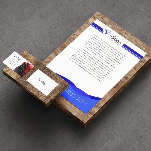 Identyfikacja wizualna firmy V-Scan: wizytówki z grafiką auta, papier firmowy z logo, całość na drewnianej podstawce, szare tło.