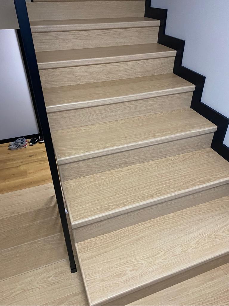 Jasne, drewniane schody z czarną balustradą, widok z dołu. Minimalistyczny design, naturalne oświetlenie, widoczne detale faktury drewna. Ukończony projekt wykończenia wnętrza.