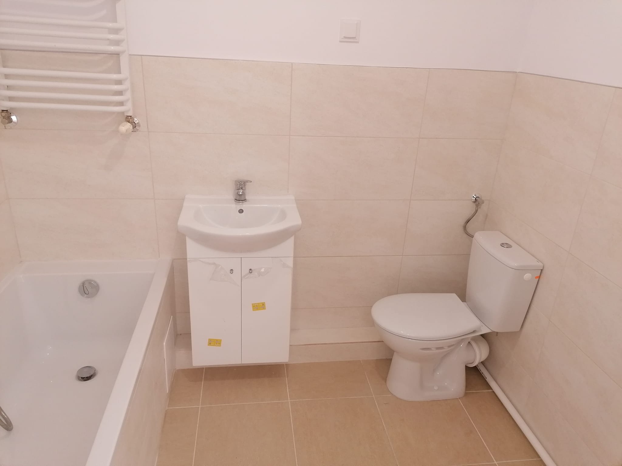 Nowoczesna, jasna łazienka w Działdowie po remoncie: biała wanna, umywalka z szafką i toaleta, beżowe płytki na ścianach i podłodze.