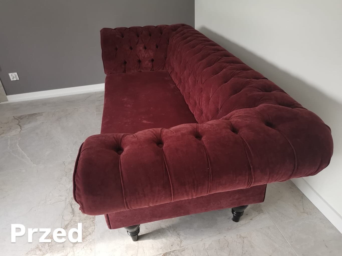 Czerwona sofa typu Chesterfield przed renowacją w Tychach. Widoczne ślady użytkowania na welurowej tapicerce i charakterystyczne pikowania.