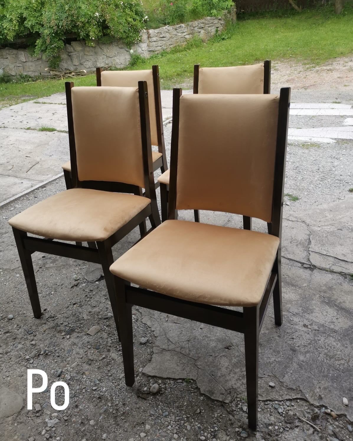 Cztery krzesła po renowacji tapicerki, z beżowym obiciem i ciemnym drewnianym stelażem, ustawione na zewnątrz na betonowym podłożu z widoczną zielenią w tle.