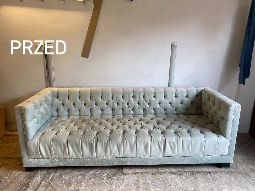 Jasnoszara sofa Chesterfield z głębokimi pikowaniami i ozdobnymi nitami, sfotografowana w kadrze 'przed' renowacją. Widoczne niedoskonałości tapicerki.