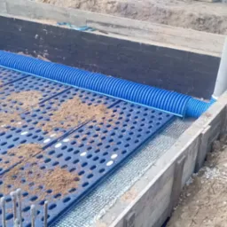 Fundament z hydroizolacją, drenażem i płytami drenażowymi, widoczny ubijak wibracyjny i drabina