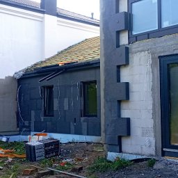 MAŁSTEF Stefan Kozeł - Budowa domu w trakcie: ocieplenie ścian grafitowym styropianem, widoczne okna z folią ochronną, więźba dachowa, białe bloczki. Prace budowlane w toku.