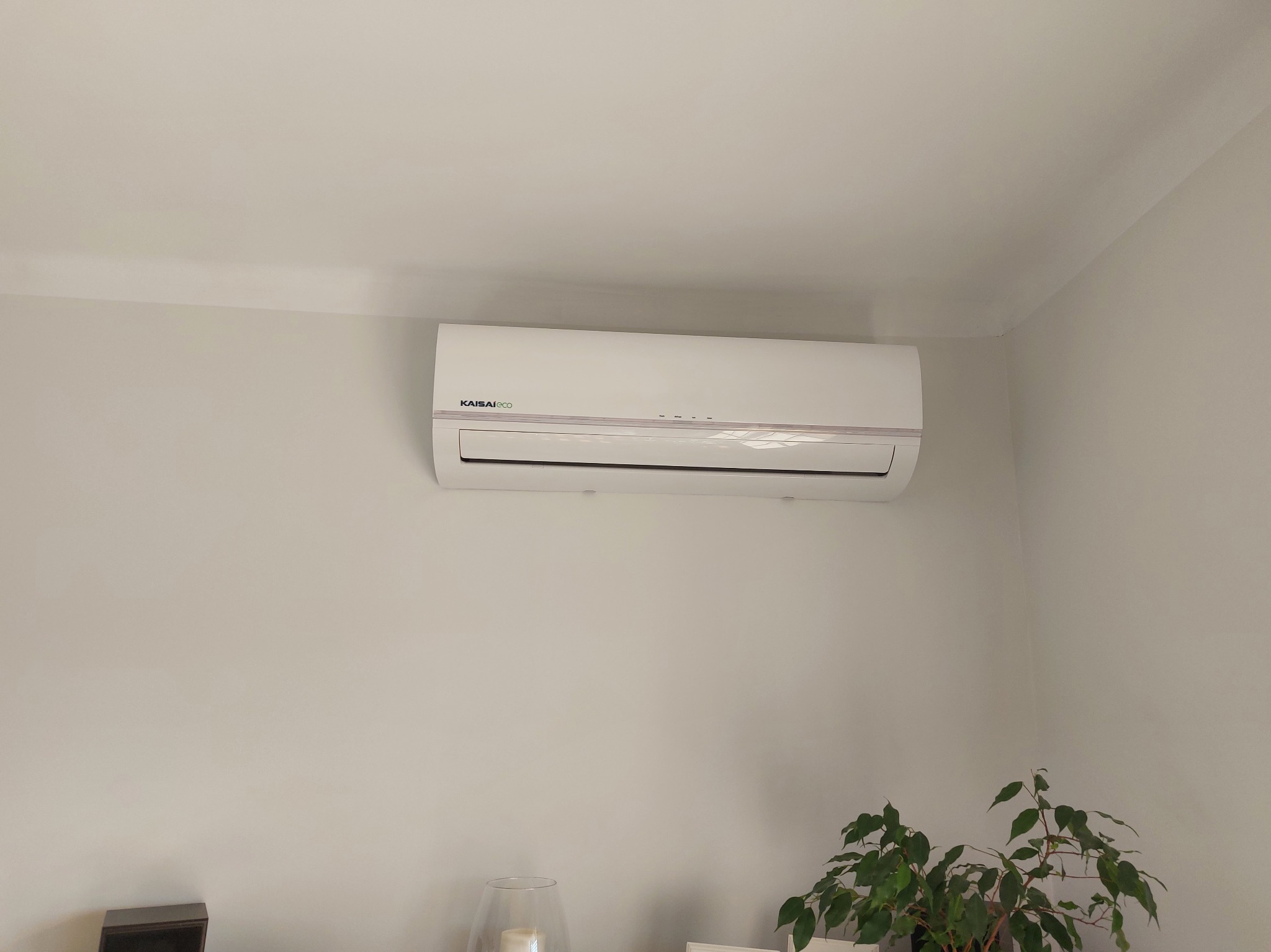 Zamontowany klimatyzator Kaisai Eco na ścianie w Dąbrowie Górniczej. Widoczny fragment rośliny doniczkowej i lampy. Jasne wnętrze, neutralne kolory ścian.