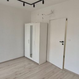 Malowanie, Szpachlowanie, Montaż mebli Gliwice i Śląsk - Jasne wnętrze pokoju po remoncie: białe ściany, drewnopodobna podłoga, biała szafa z lustrami i drzwi. Minimalistyczne oświetlenie sufitowe.
