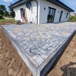 NETCORE CONNECT SPÓŁKA Z OGRANICZONĄ ODPOWIEDZIALNOŚCIĄ - Nowoczesny taras z szarej kostki brukowej ułożonej w geometryczny wzór, z widocznym obrzeżem i przygotowanym terenem pod dalsze prace wykończeniowe.