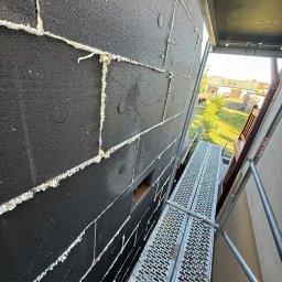 FIRMA HANDLOWO-USŁUGOWA DAMIAN GRODECKI - Czarny styropian na elewacji budynku w Nowej Wsi, przyklejony pianką montażową. Widok z rusztowania, z boku. Etap ocieplania.