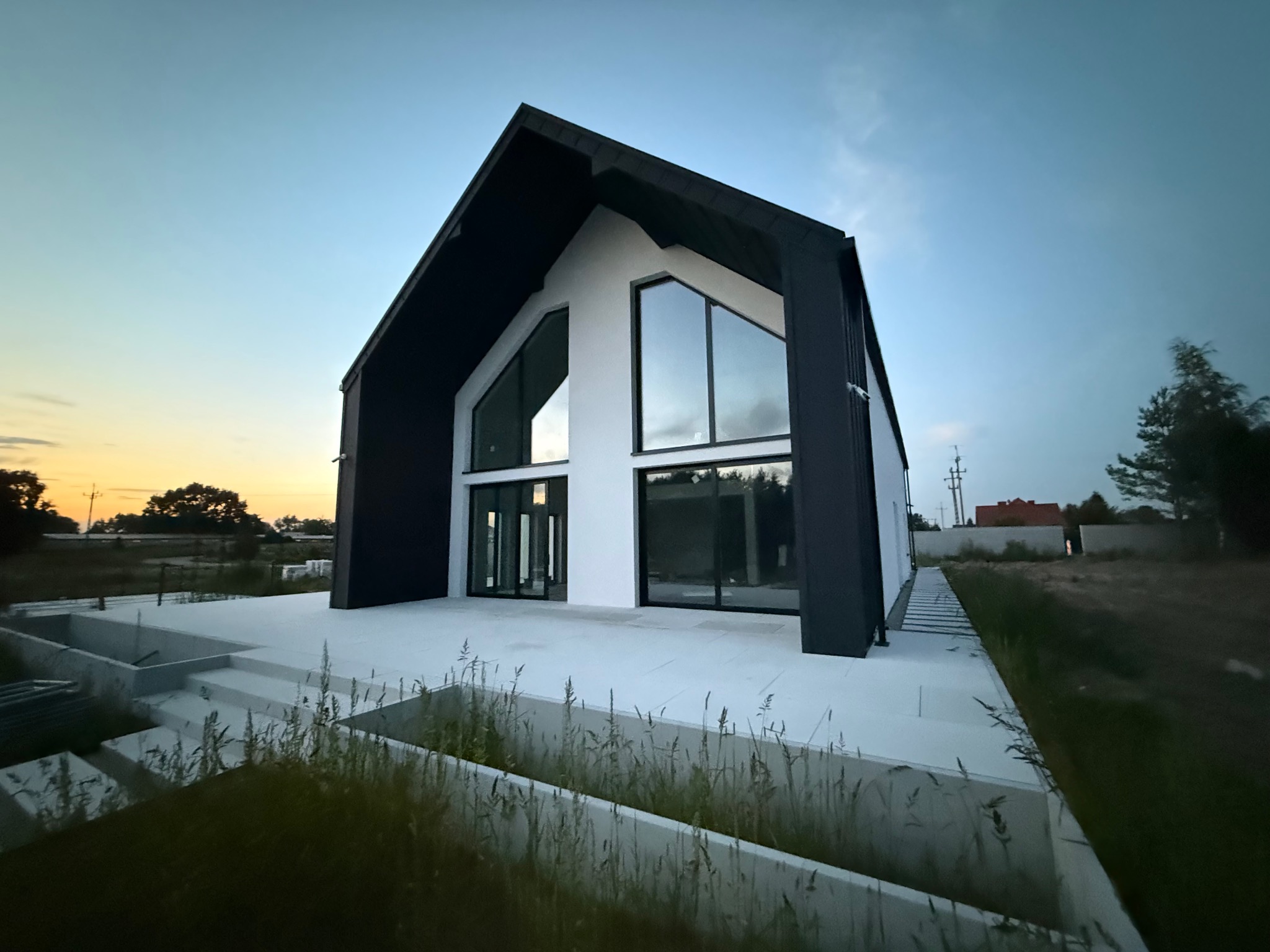 Nowoczesny dom z czarno-białą elewacją i dużymi oknami, sfotografowany o zmierzchu. Widoczne elementy wykończeniowe i minimalistyczny design.