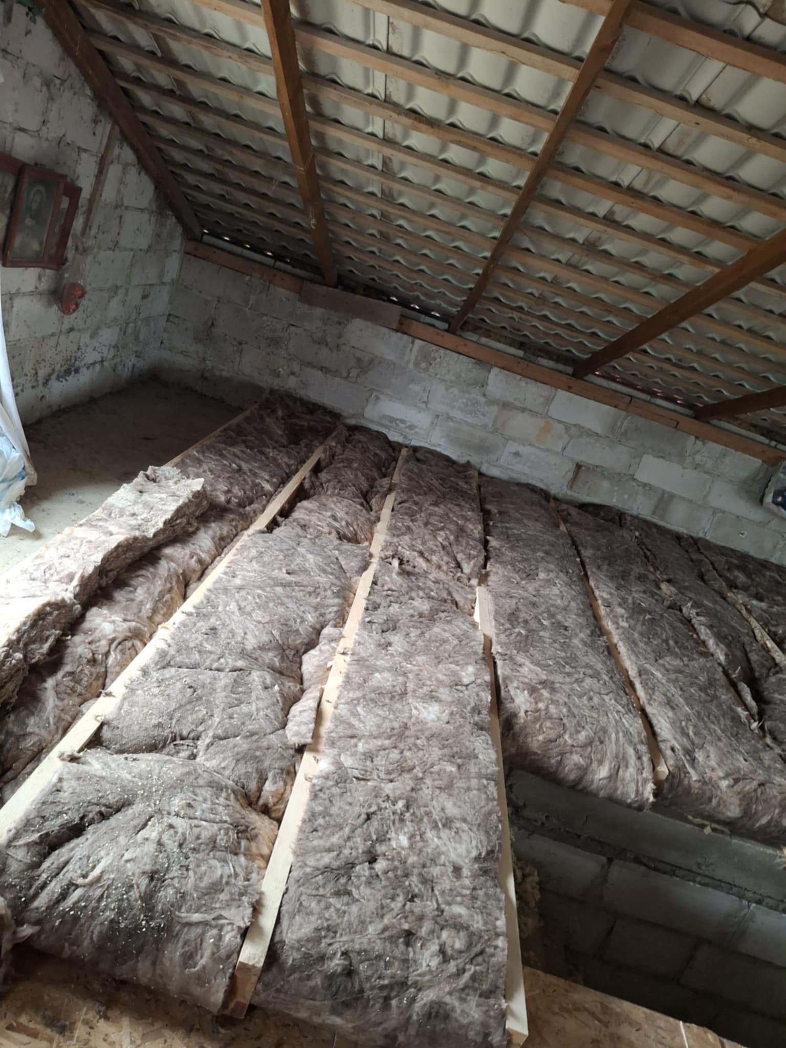 Poddasze z widoczną izolacją z wełny mineralnej między krokwiami. Surowy stan, cegły i drewniana konstrukcja dachu. Ujęcie z dołu, perspektywa zbieżna.