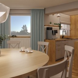 Flow Studio Projektowe Ewa Zarazińska - Jasna kuchnia z drewnianymi akcentami, okrągły stół z wazonem i filiżankami, krzesła z krzyżowym oparciem, nowoczesna lampa wisząca, okno z błękitnymi zasłonami.