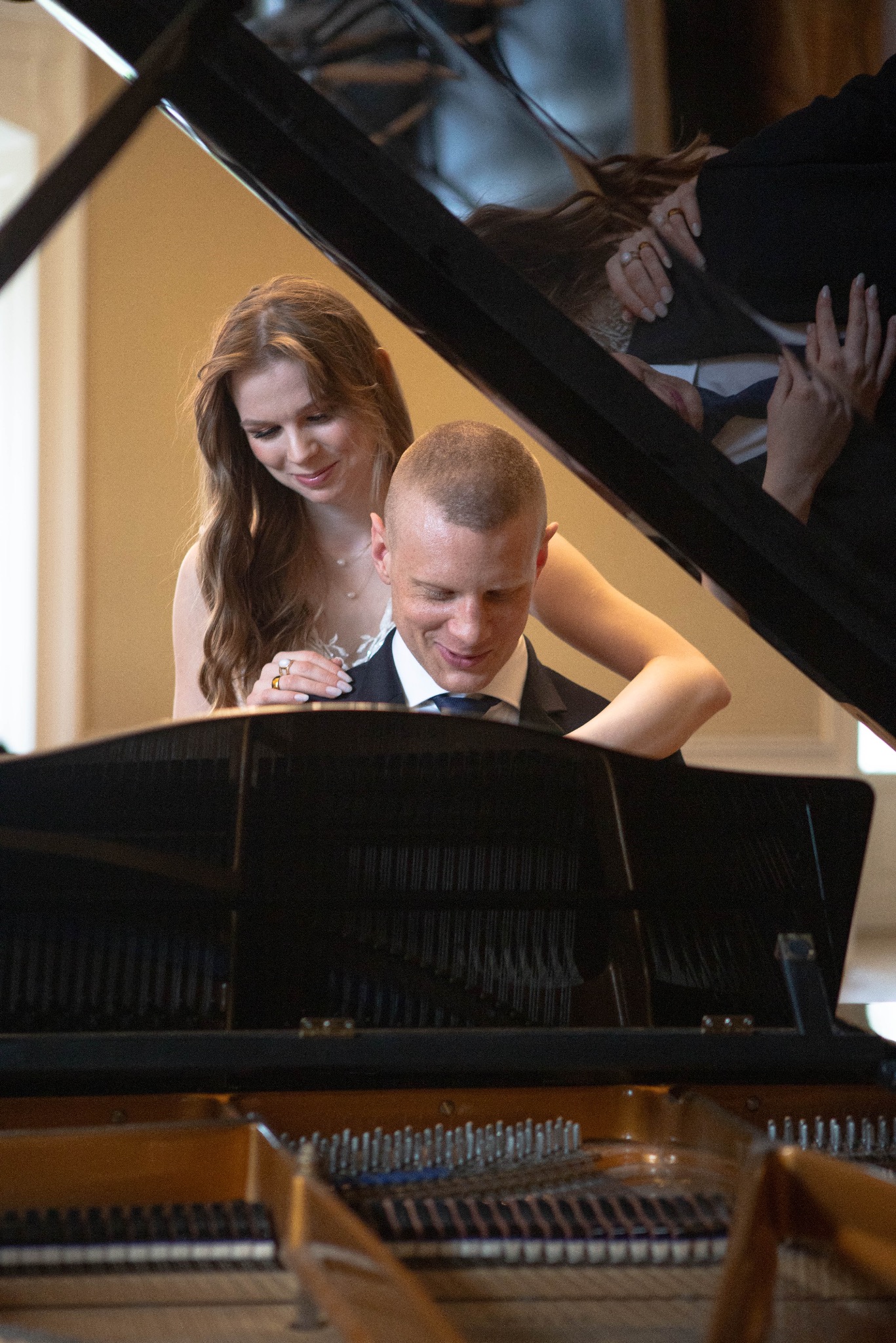 Para młoda przy fortepianie: panna młoda obejmuje pana młodego, który gra. Ujęcie z bliska, widoczne detale instrumentu i obrączki.