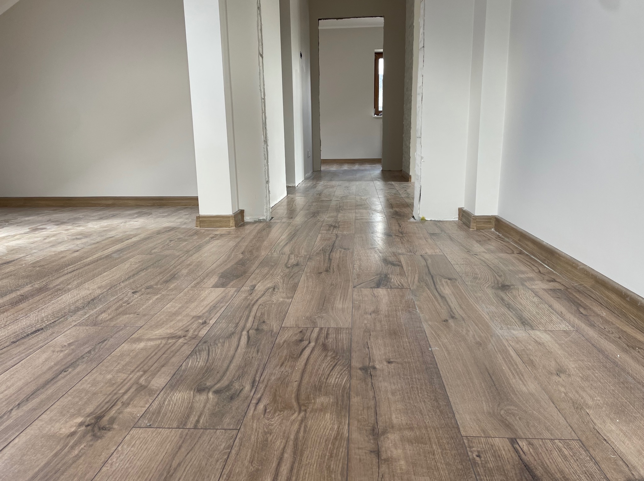 Ułożona podłoga z paneli imitujących drewno w korytarzu z białymi ścianami i kolumnami. Widok w perspektywie, z niskiego kąta, podkreślający wzór podłogi.
