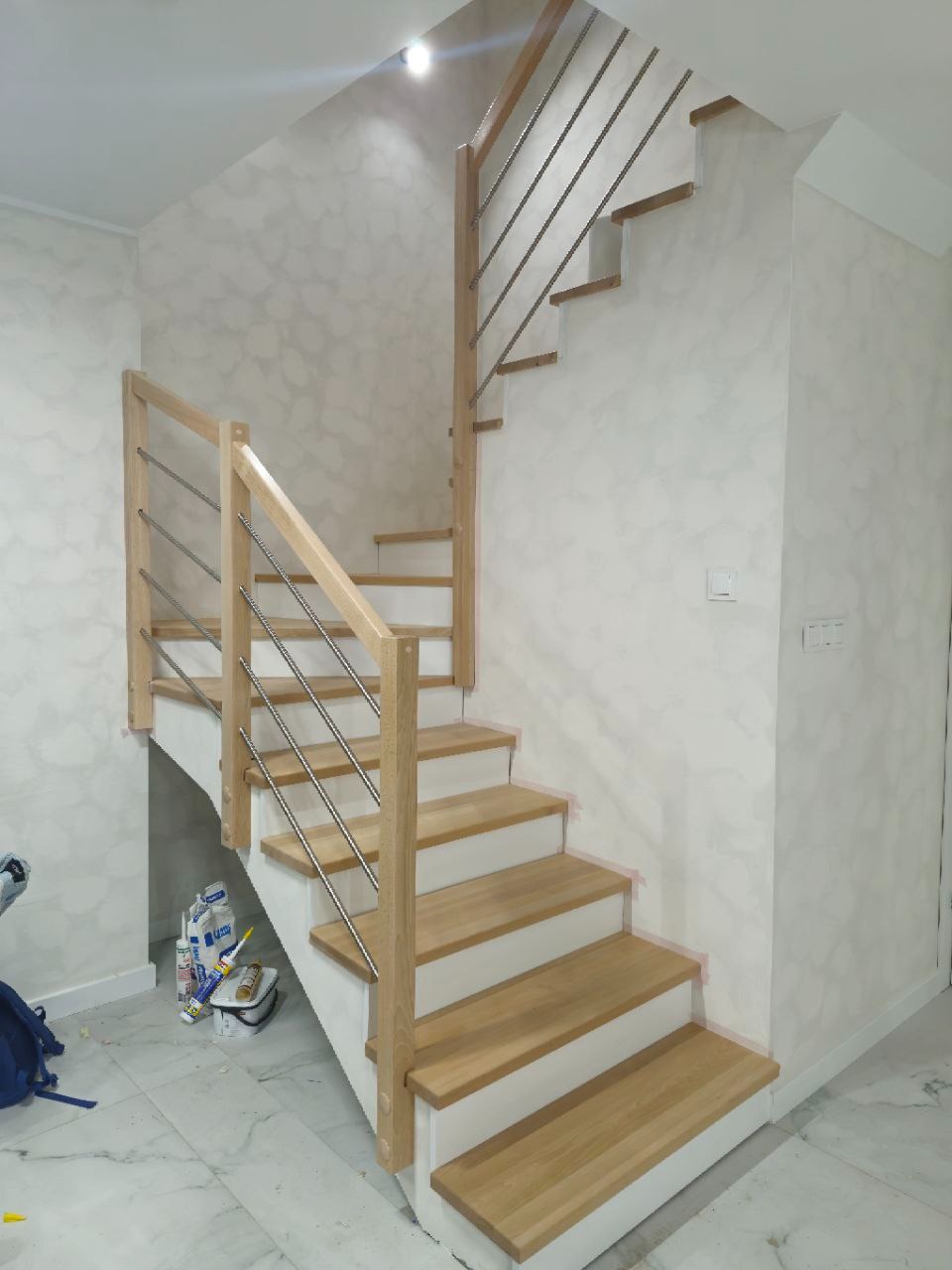 Jasne schody z drewnianymi stopniami i metalową balustradą w nowoczesnym wnętrzu. Widok z dołu, podkreślający minimalistyczny design i jasną kolorystykę.