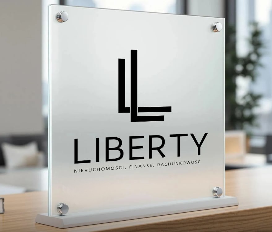 Szklany szyld z logo firmy 'Liberty' oferującej usługi z zakresu nieruchomości, finansów i rachunkowości, umieszczony na drewnianym biurku w jasnym biurze.