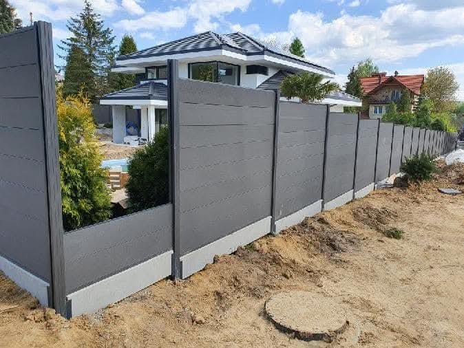Nowoczesne ogrodzenie panelowe w kolorze szarym, z widoczną konstrukcją i betonową podmurówką, na tle domu z basenem i zielenią. Ujęcie z poziomu gruntu.