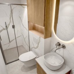 17 Studio Projektowe Sylwia Bierwiaczonek - Nowoczesna łazienka z kabiną prysznicową, umywalką nablatową i podświetlanym lustrem. Marmurowe płytki na ścianach i drewniane szafki dodają elegancji.