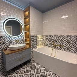 17 Studio Projektowe Sylwia Bierwiaczonek - Nowoczesna łazienka z owalną umywalką na szarej szafce z drewnianym blatem, okrągłe lustro z podświetleniem LED i wolnostojąca wanna na tle wzorzystych płytek.