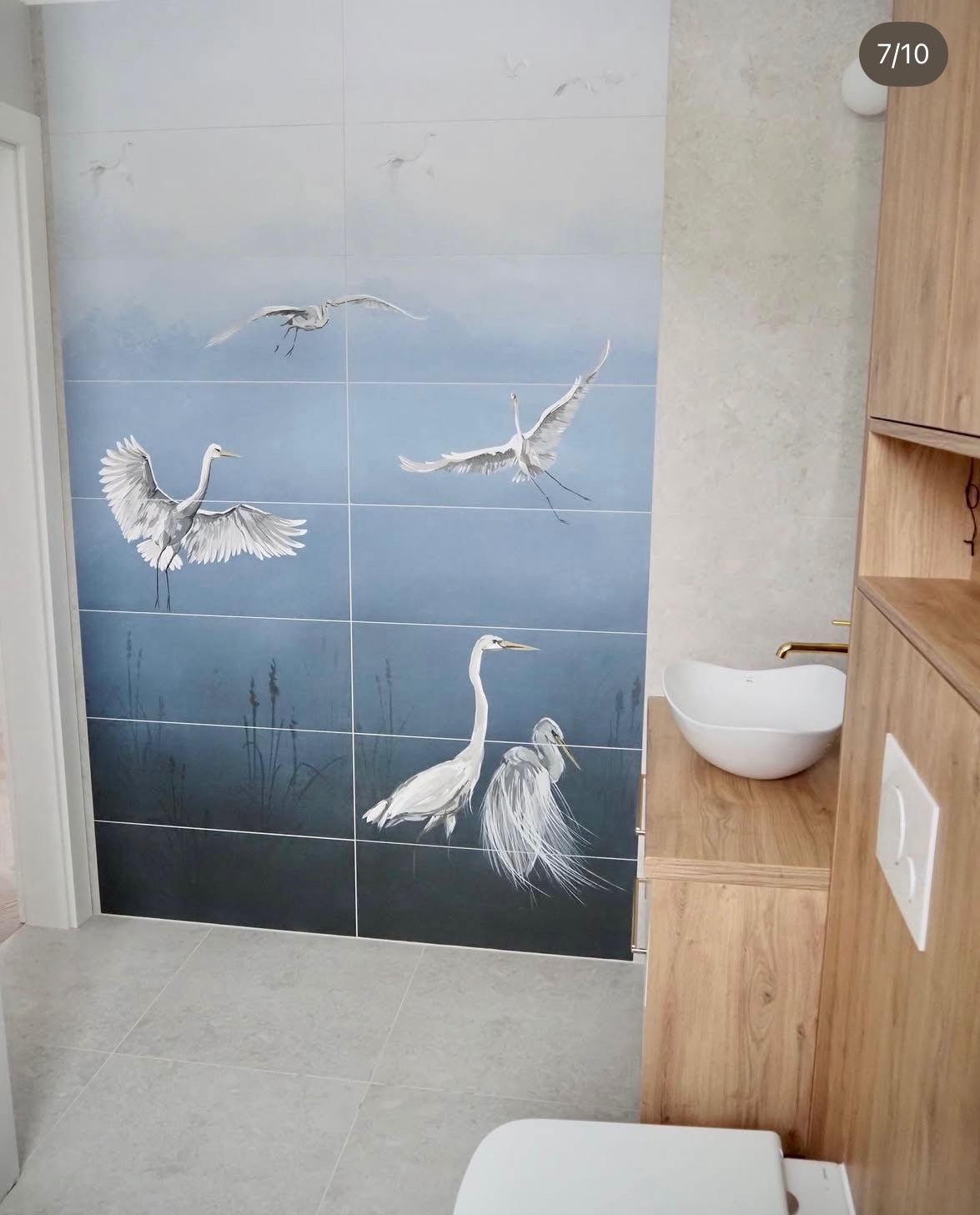 Wykończona łazienka z płytkami z motywem czapli, umywalką nablatową i drewnianą szafką. Nowoczesny design z akcentem natury.