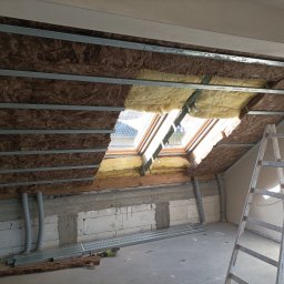 Mateusz Borowski - Izolacja poddasza wełną mineralną, widoczne profile metalowe i okno dachowe. Częściowo ocieplone, drabina oparta o ścianę. Prace wykończeniowe w toku.