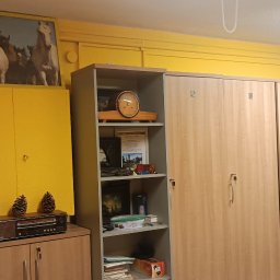 Patryk Buczkowski - Żółta szatnia z drewnianymi szafkami, numerowanymi od 1 do 7. Na szafkach dekoracje: radio retro, szyszki, obraz z końmi. Ściany i sufit pomalowane na żółto.