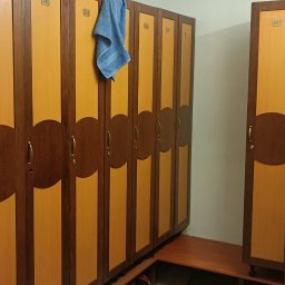 Patryk Buczkowski - Szereg drewnianych szafek z numerami w szatni, z niebieskim ręcznikiem wiszącym na jednej z nich. Pod szafkami widoczne buty.