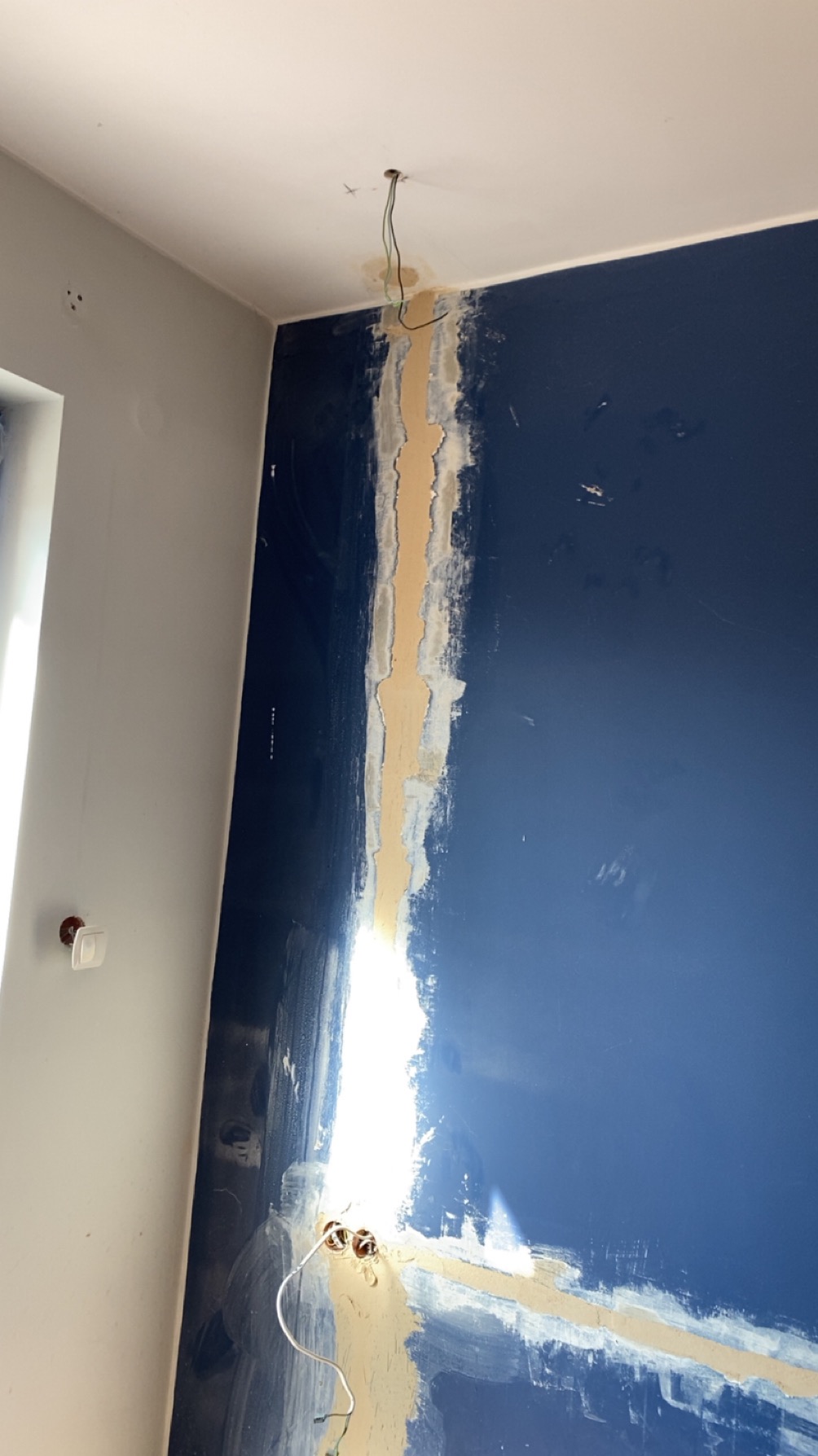 Niebieska ściana z wyżłobieniami pod instalację elektryczną, przygotowana do szpachlowania. Widoczne kable i puszki elektryczne. Ujęcie z dołu, sufit w rogu kadru.