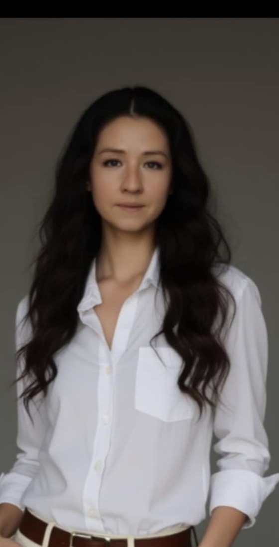 Portret kobiety w białej koszuli na szarym tle. Zdjęcie profilowe pracownika biura w Warszawie, sugerujące profesjonalizm i otwartość.