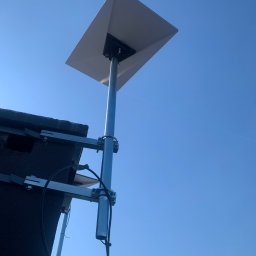 Yehor Chebotar - Antena satelitarna zamontowana na dachu budynku, widoczna na tle błękitnego nieba. Metalowa konstrukcja wspornika, kabel antenowy. Ujęcie z dołu.