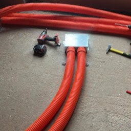 KWD-INSTAL SPÓŁKA Z OGRANICZONĄ ODPOWIEDZIALNOŚCIĄ - Montaż instalacji ogrzewania podłogowego w Warszawie: pomarańczowe rury w peszlu, narzędzia pracy i okno w tle. Etap prac przed wylaniem posadzki.