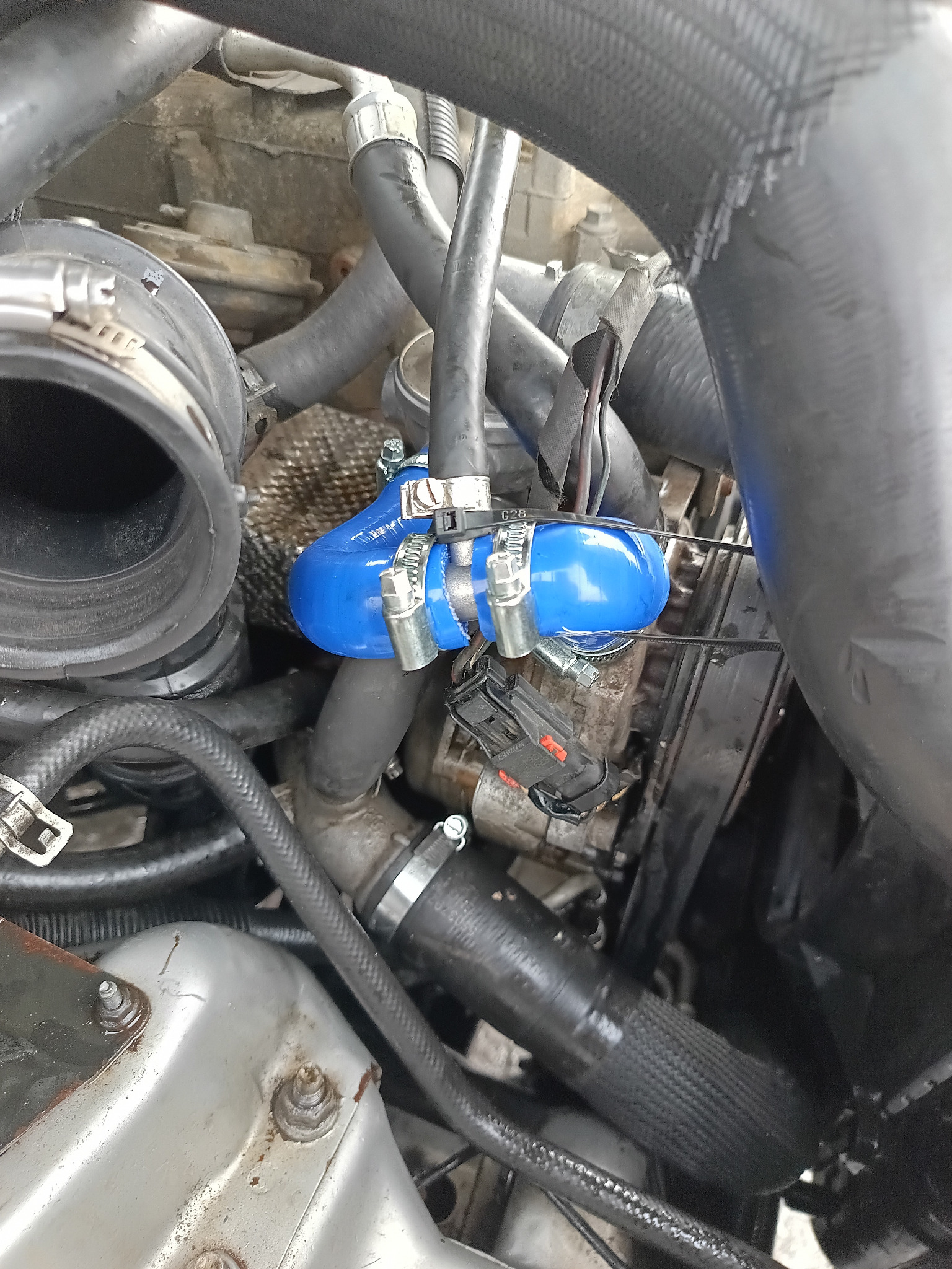 Silnik samochodowy z nowym, niebieskim przewodem zamocowanym za pomocą metalowych zacisków. Widoczne inne elementy silnika i przewody.