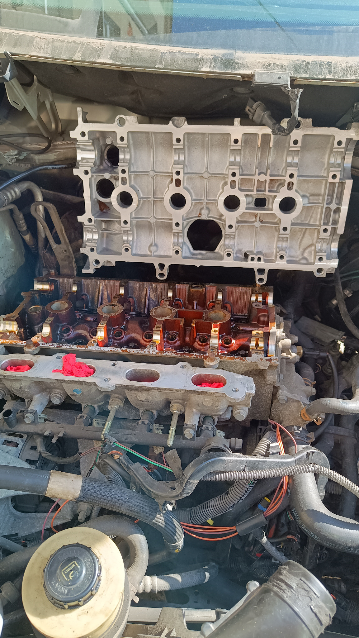 Silnik samochodowy w trakcie naprawy: zdemontowana głowica, widoczne elementy wewnętrzne, zabezpieczone otwory. Detaliczny widok na proces naprawy.