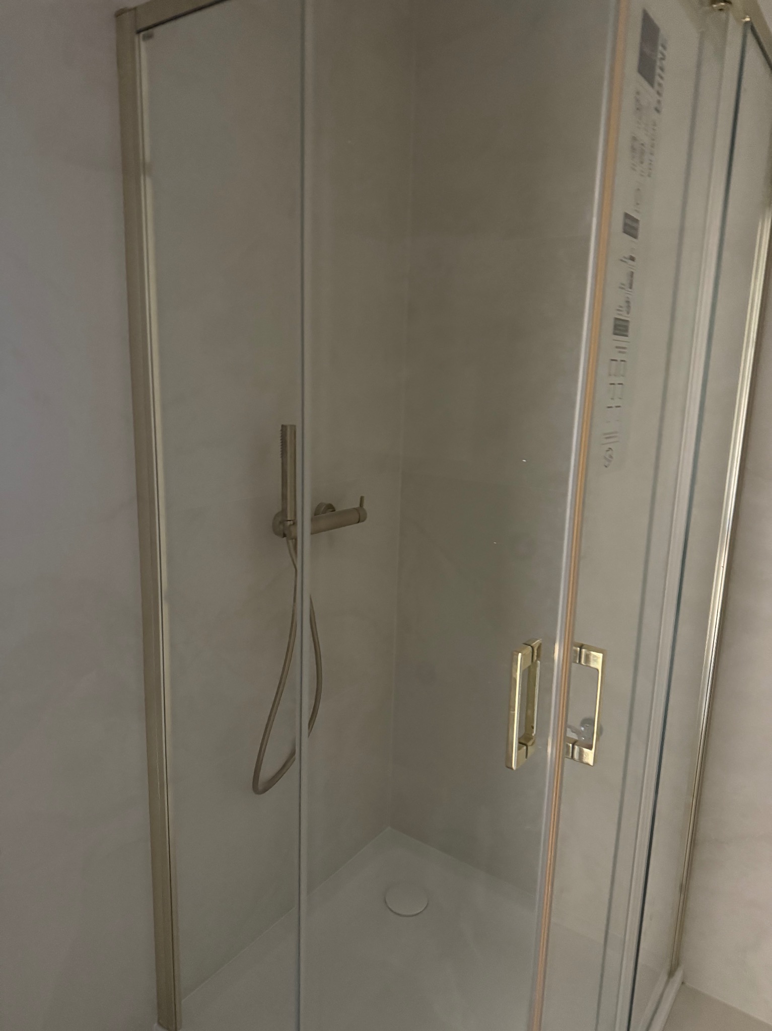 Szklana kabina prysznicowa z chromowanymi okuciami i złotymi uchwytami, zamontowana w jasnej łazience. Widoczny zestaw prysznicowy.