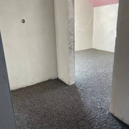 HMS PRO IVAN PORTIANYK - Wylewka anhydrytowa na podłodze w surowym wnętrzu z widoczną instalacją elektryczną. Różowy sufit poddasza w tle. Widok zza framugi drzwi.