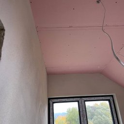 HMS PRO IVAN PORTIANYK - Pokój w trakcie wykańczania: ściana po szpachlowaniu, sufit z płyt kartonowo-gipsowych w kolorze różowym, okno z widokiem na drzewa.