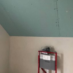 HMS PRO IVAN PORTIANYK - Montaż stelaża WC TECE na tle ściany i sufitu z płyt gipsowo-kartonowych. Widoczne łączenia płyt i otwory po wkrętach. Ujęcie z dołu, widać skos sufitu.