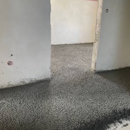 HMS PRO IVAN PORTIANYK - Wylewka anhydrytowa na podłodze w surowym wnętrzu z widocznymi przewodami elektrycznymi w ścianie i oknem dachowym. Szara, chropowata powierzchnia w trakcie realizacji.