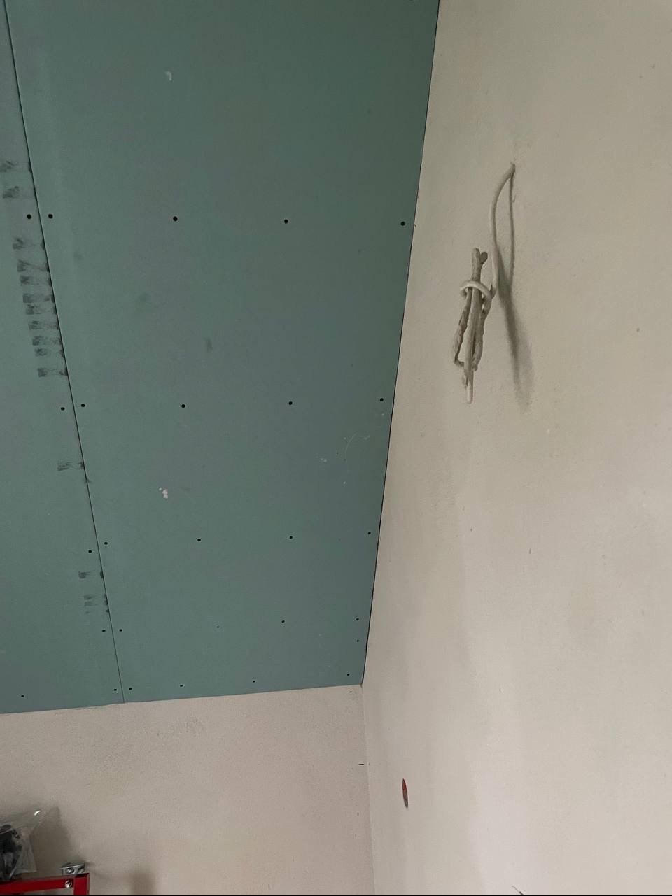 Płyta gipsowo-kartonowa na suficie, widoczne łączenia i wkręty. Na ścianie wystające przewody elektryczne. Przygotowanie do szpachlowania i malowania.