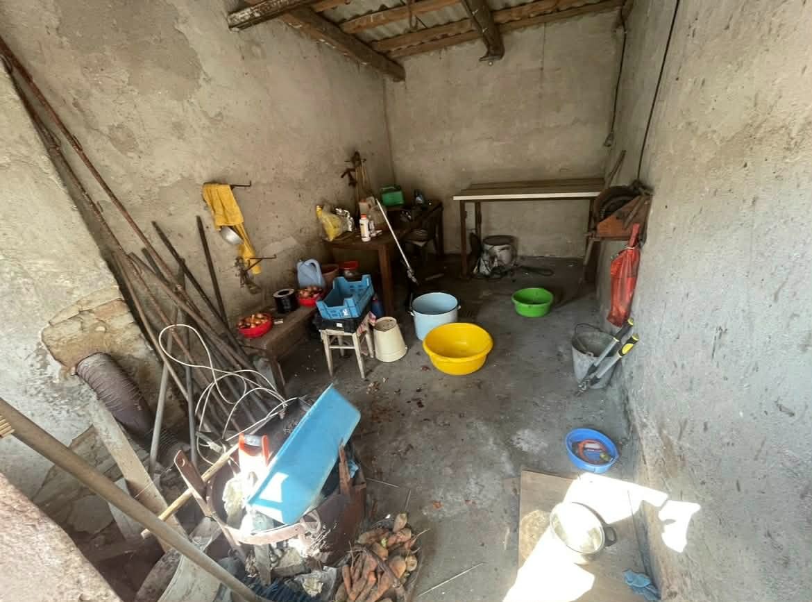 Zaniedbane pomieszczenie gospodarcze z narzędziami i wiadrami, przygotowane do uprzątnięcia. Widoczne stare ściany i prowizoryczne wyposażenie.