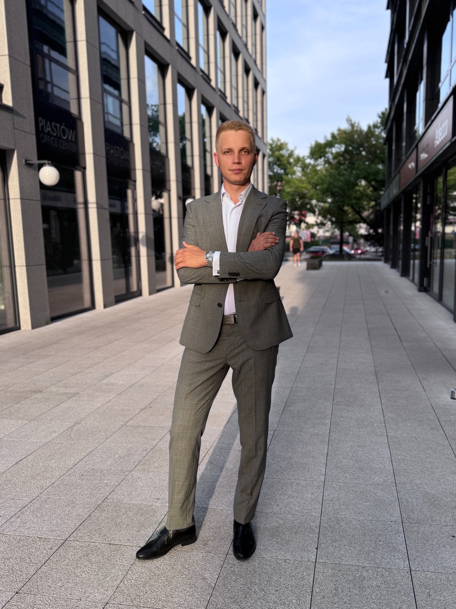 Mężczyzna w garniturze na tle nowoczesnej architektury miejskiej. Ujęcie z dołu, podkreślające sylwetkę i otoczenie biurowców.