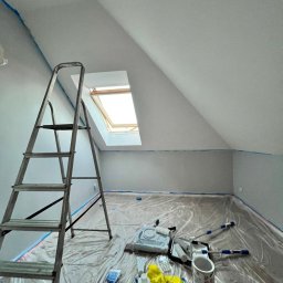 Amelia Szuba - Pokój na poddaszu w trakcie malowania: zabezpieczona folią podłoga, drabina oparta o ścianę, okno dachowe, widoczne narzędzia malarskie i taśma malarska.