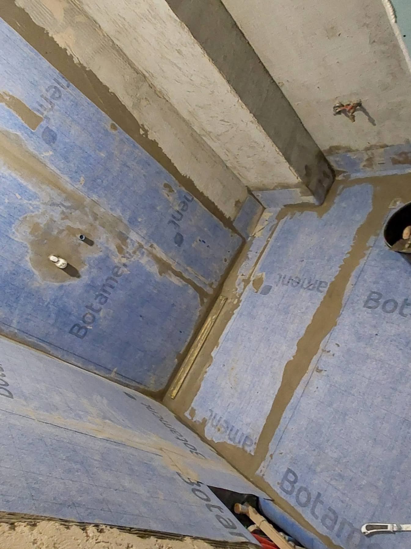 Hydroizolacja w rogu łazienki z użyciem folii w płynie Botament, zabezpieczająca przed wilgocią, z widocznymi detalami uszczelnienia i przygotowania podłoża.
