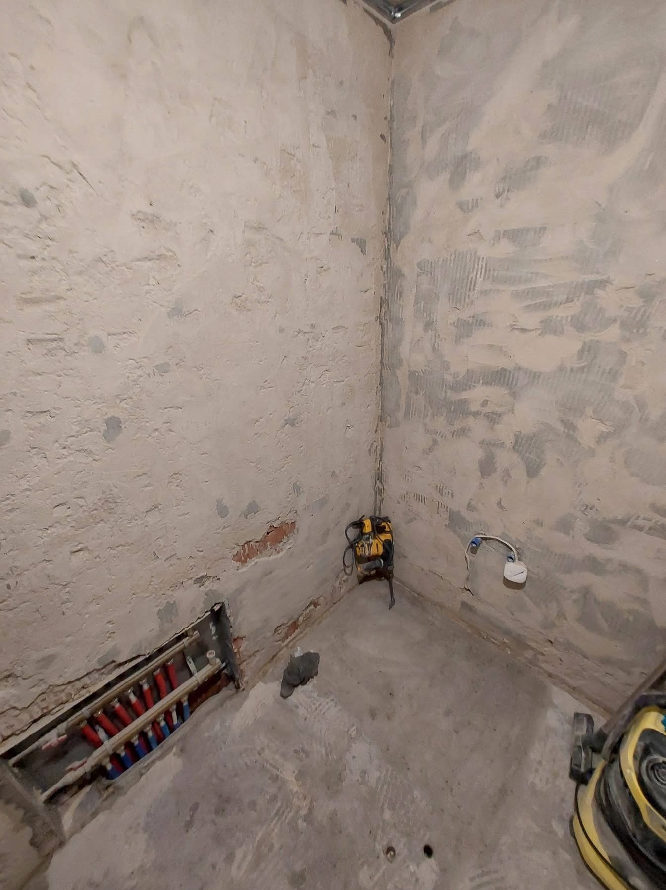 Surowe ściany w trakcie remontu z widoczną instalacją grzewczą w podłodze i narzędziami, ukazujące etap prac przygotowawczych przed wykończeniem.