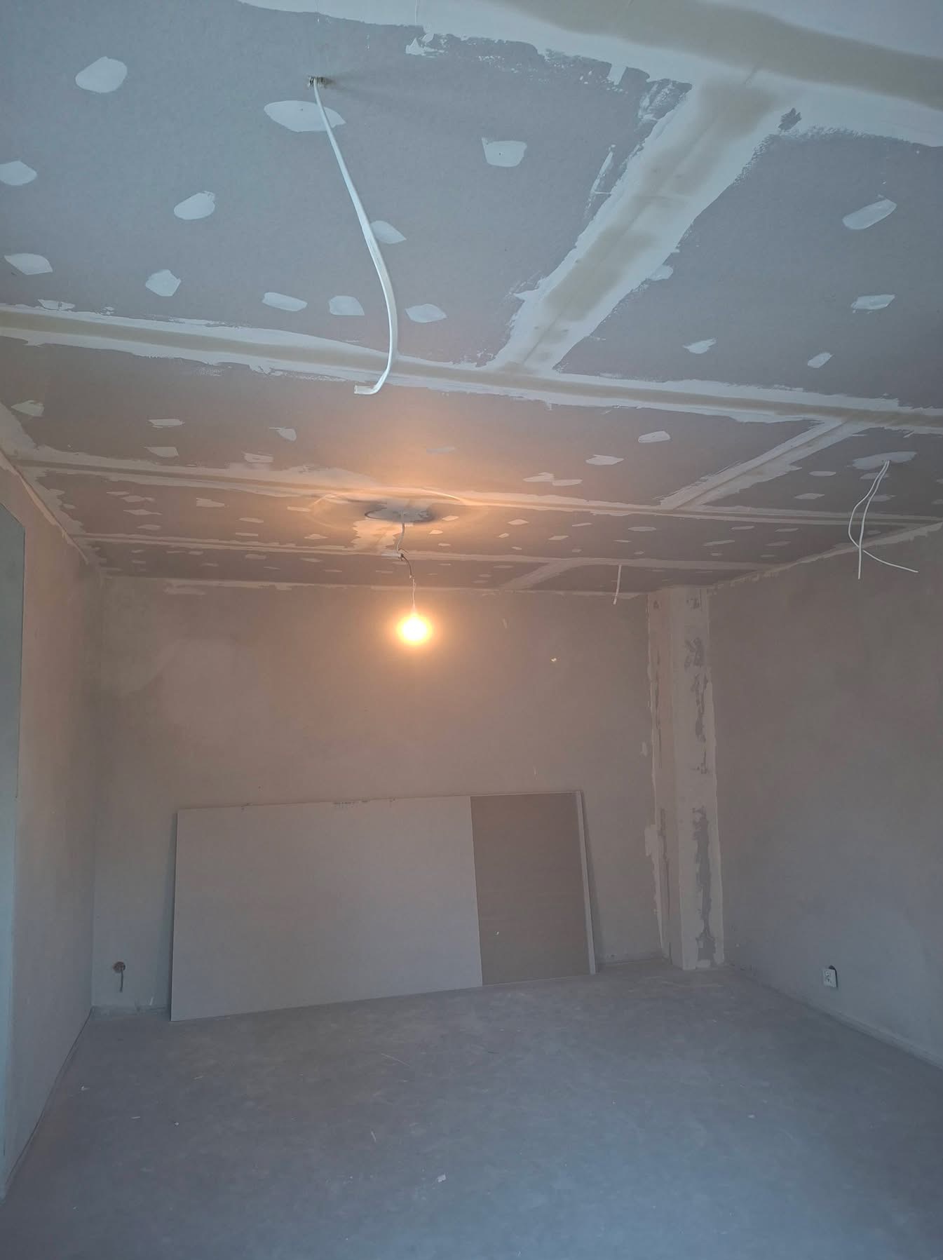 Wnętrze w trakcie prac wykończeniowych: sufit z płyt karton-gips, widoczne łączenia i szpachlowanie, wiszące przewody elektryczne, przygotowanie do dalszych prac.