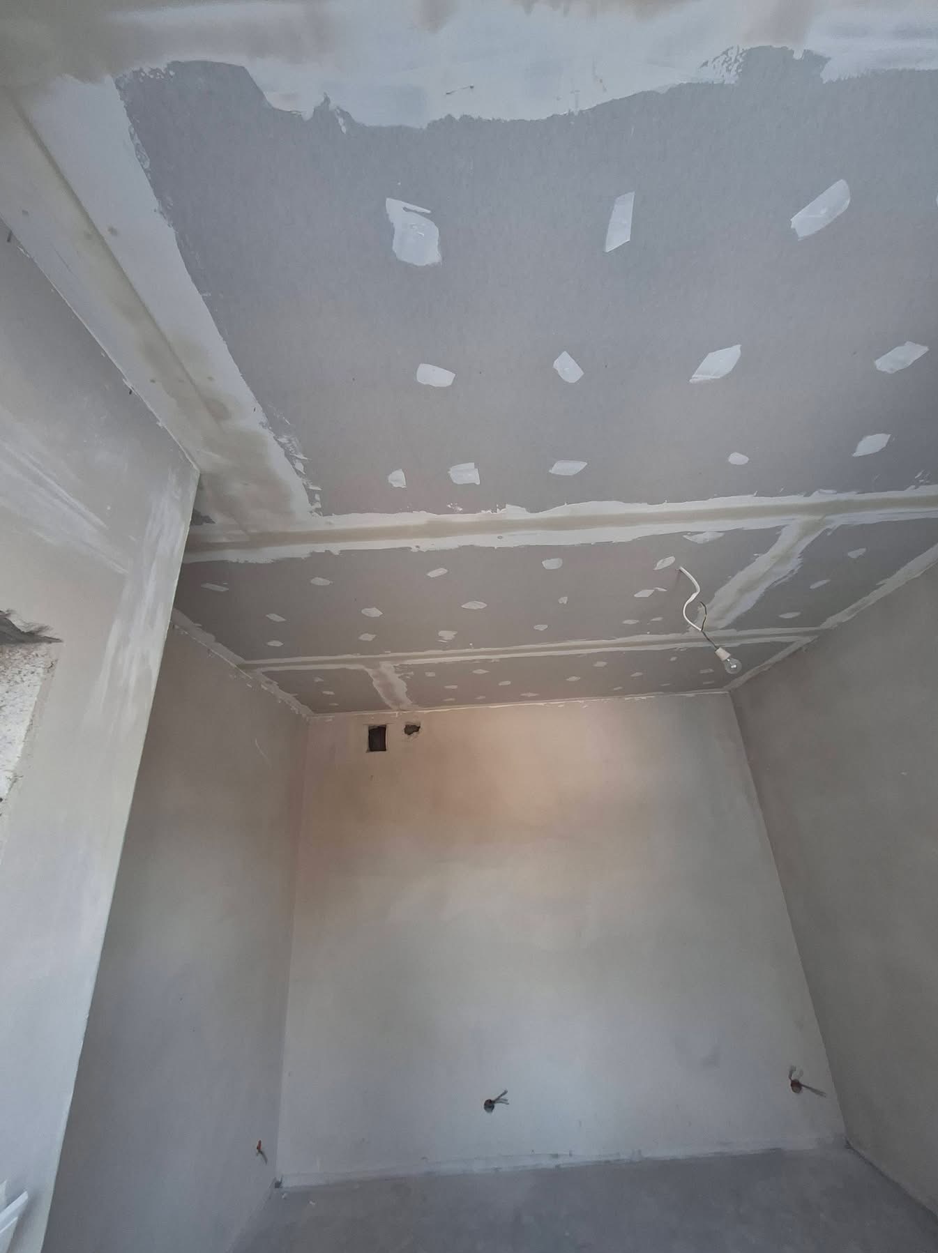 Pokój w trakcie szpachlowania: sufit z płyt karton-gips, widoczne łączenia i miejsca po wkrętach, ściany przygotowane do dalszych prac wykończeniowych.