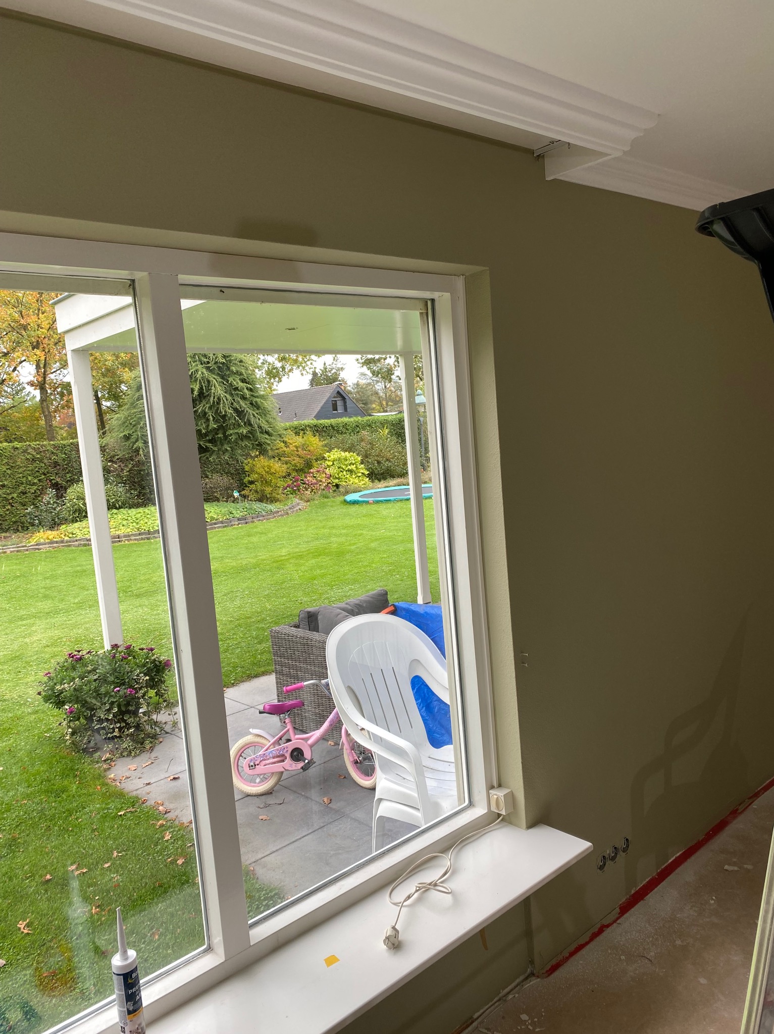 Wnętrze z oknem na ogród. Świeżo pomalowana ściana w odcieniach zieleni z zamontowaną listwą przysufitową. Widoczne gniazdka elektryczne i kabel.