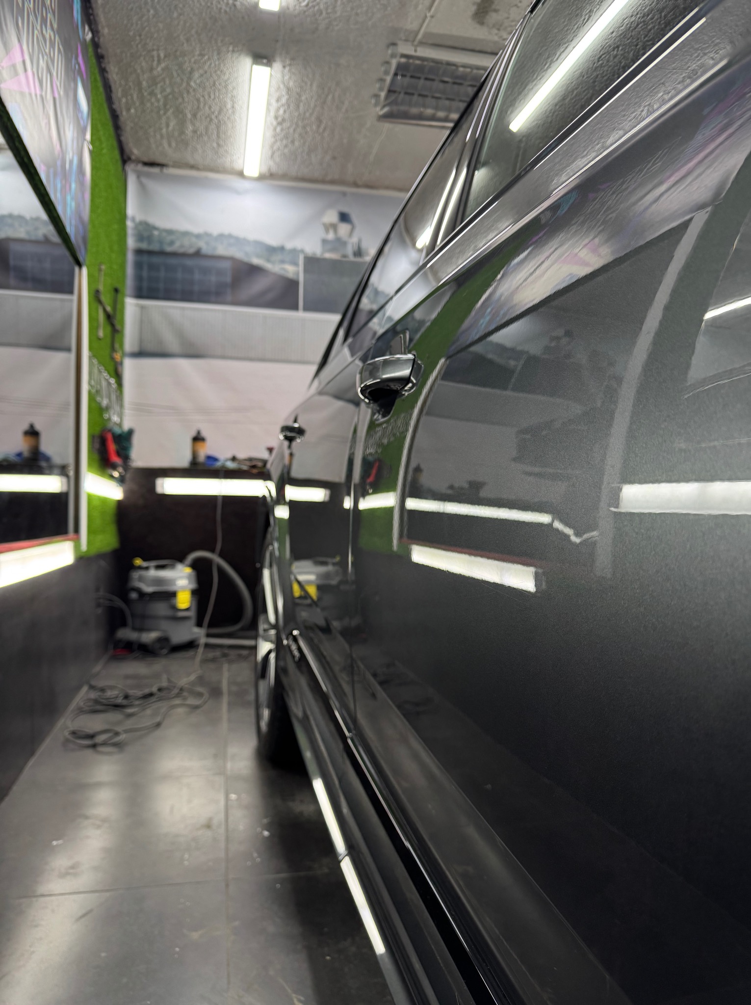 Błyszczący, szary samochód po detailingu w myjni. Widoczne odbicia światła na lakierze, odzwierciedlające czystość. W tle narzędzia i akcesoria do pielęgnacji aut.