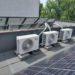 BARTCOMP - Trzy białe jednostki zewnętrzne klimatyzacji LG Smart Inverter, zamontowane na betonowych podstawach na płaskim dachu, z widocznymi rurami izolacyjnymi i panelami fotowoltaicznymi w tle.